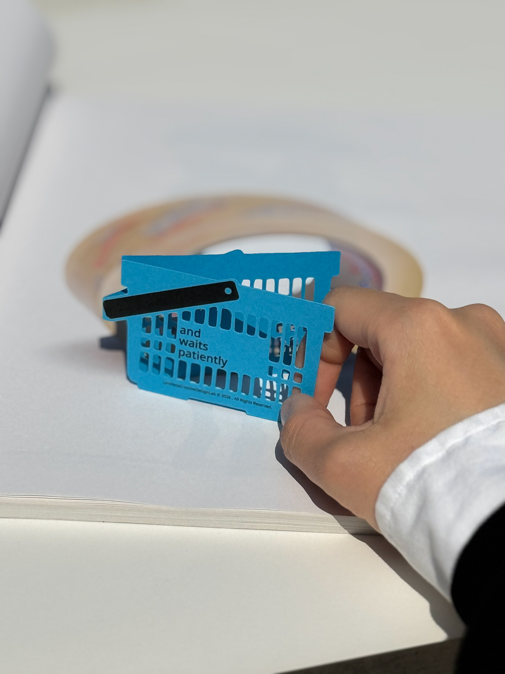 A blue shopping-basket bookmark held in a hand, showing its cut-out structure.