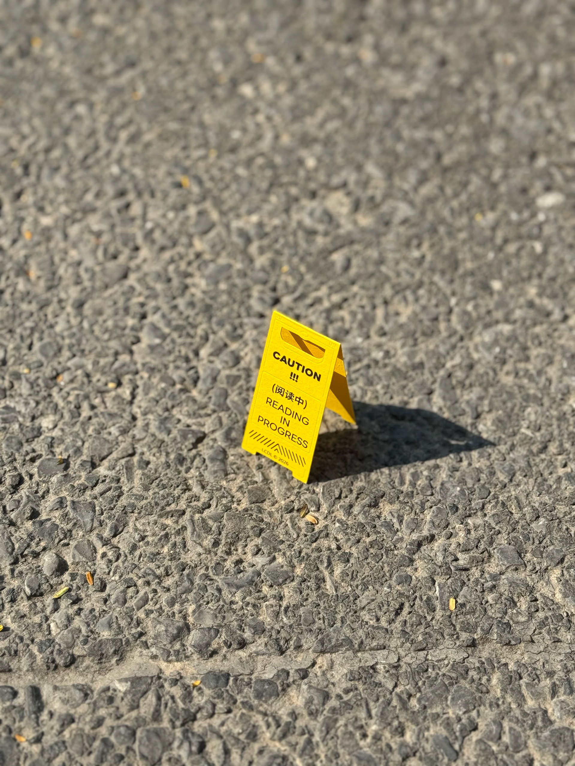 A yellow CAUTION bookmark standing on textured ground.