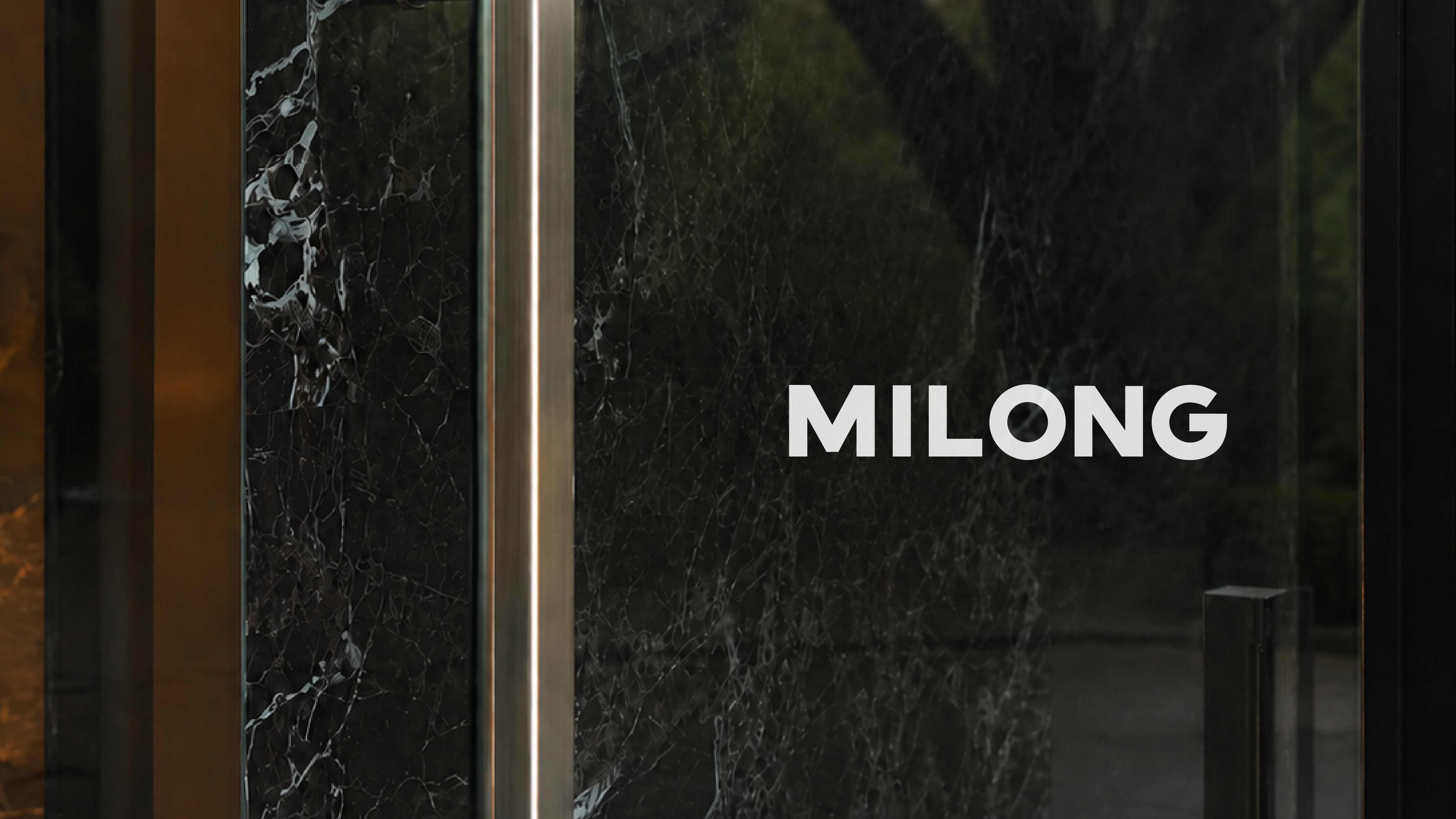 White MILONG wordmark applied to a dark glass door.