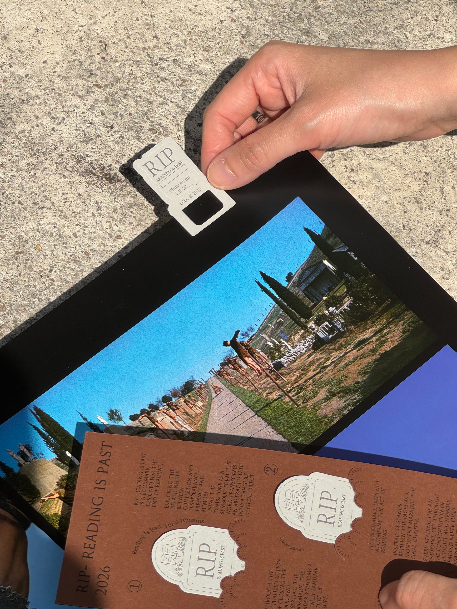 A gravestone-shaped RIP bookmark being placed between book pages.